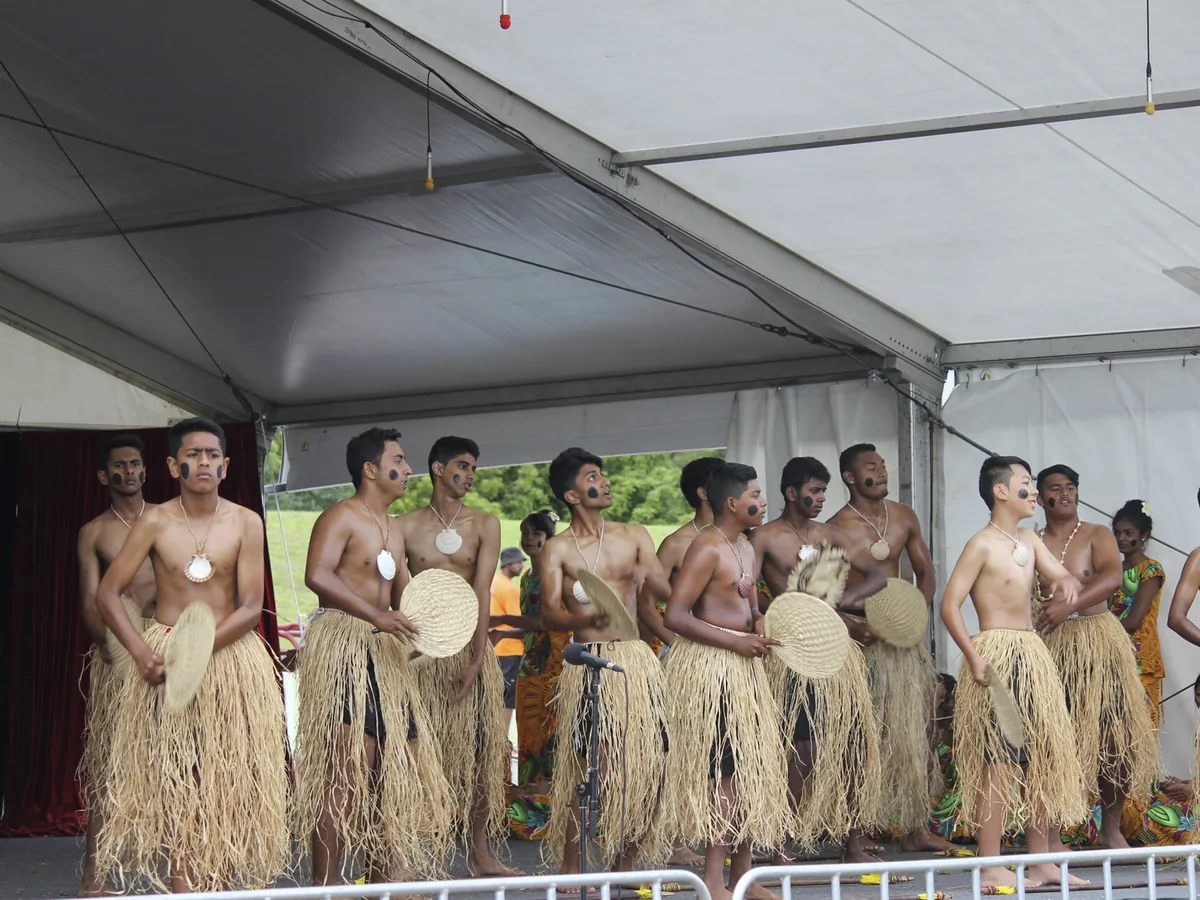 Performers in traditional Fijian dress with woven fans, seen from a wider angle on stage